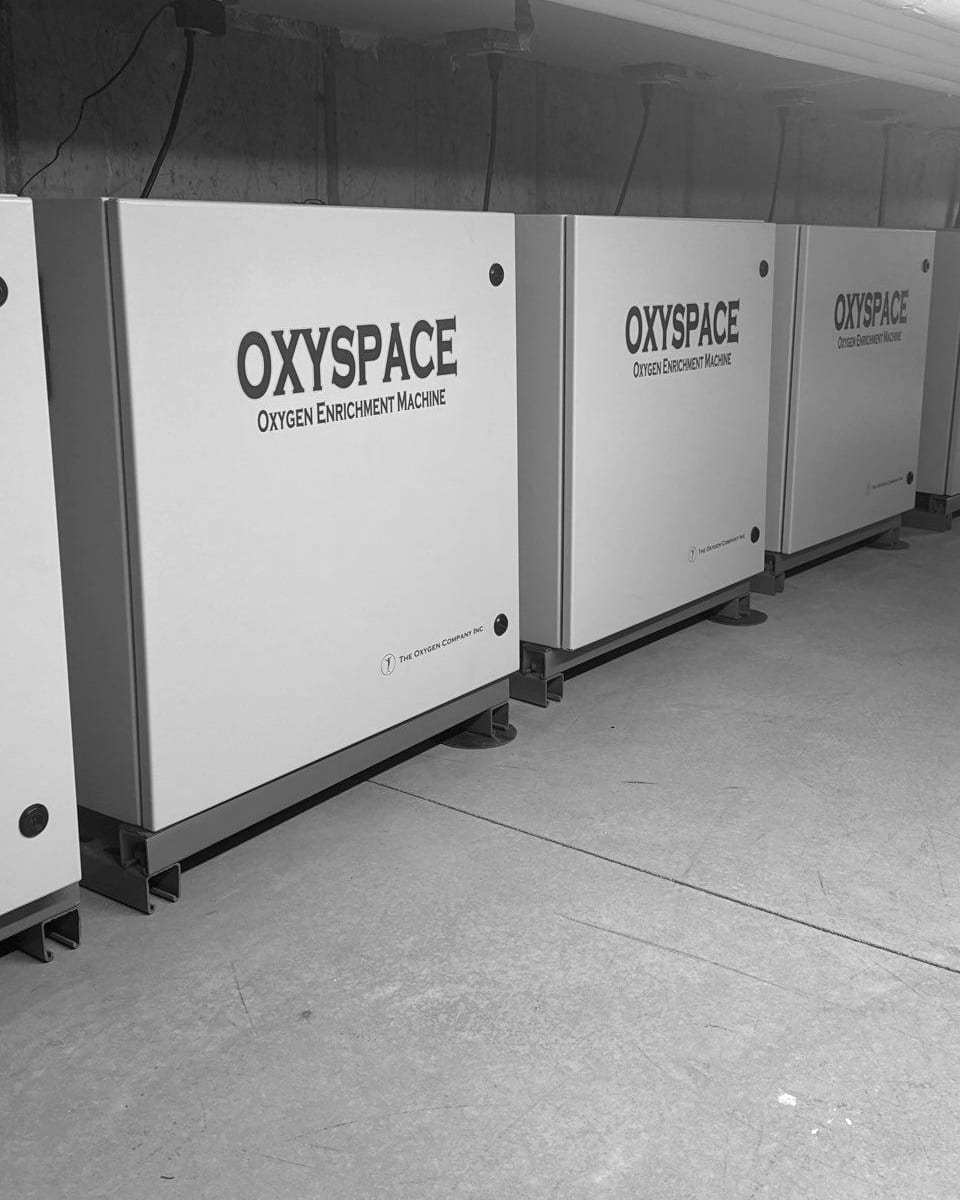 A long row of OxySpace oxygen enrichment machines, made by The Oxygen Company, Inc., installed along a mechanical room wall.