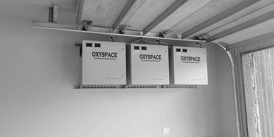 Three OxySpace oxygen enrichment machines hung on a steel service rail under a timber and steel ceiling.