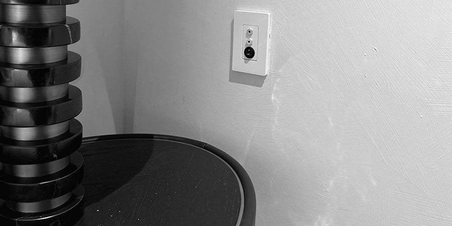 A cream oxygen outlet plate with two ports and a round fitting, above a black and brass bedside table.