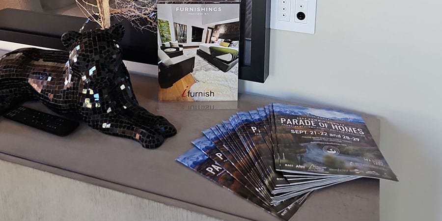 An oxygen outlet plate on a wall above a side table with Parade of Homes brochures, a furnishings catalogue and a mosaic cat figure.