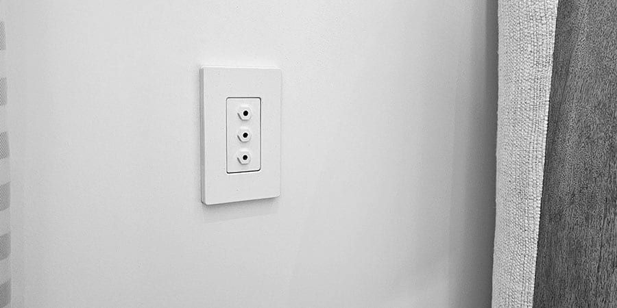 A three-port oxygen outlet plate on a beige wall beside an upholstered headboard.