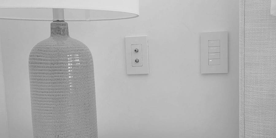 A two-port oxygen outlet plate on a bedroom wall beside a pale blue ceramic lamp and a light switch.